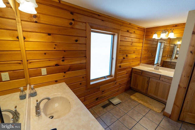 full bathroom featuring tile patterned floors, two vanities, wood walls, and a sink