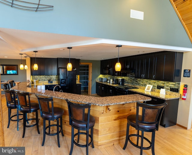 kitchen with black appliances, tasteful backsplash, dark cabinetry, light wood-style floors, and light stone countertops