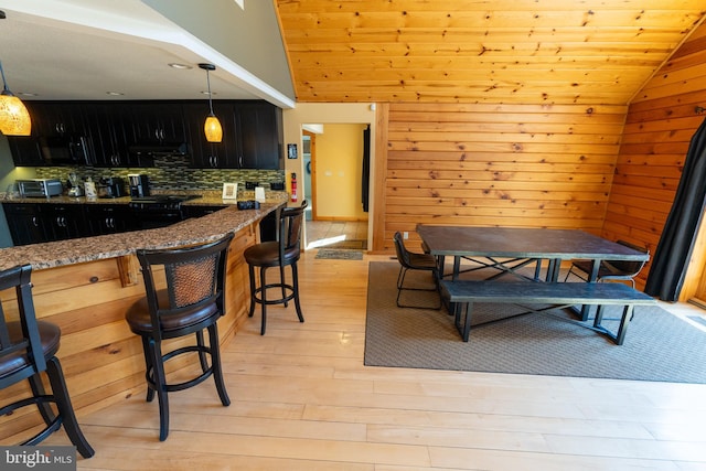 dining room with wooden walls, wooden ceiling, light wood-style floors, and vaulted ceiling