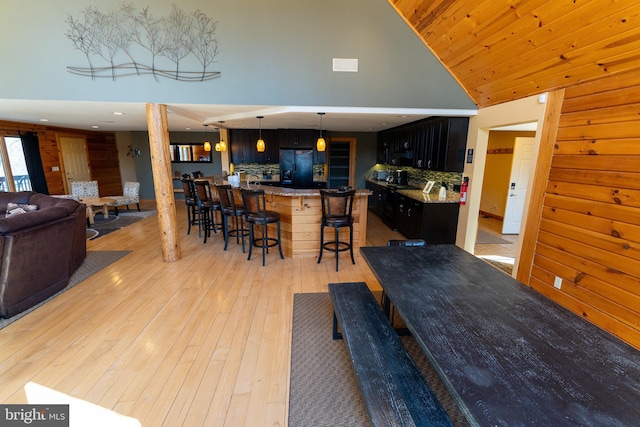 interior space with light wood-type flooring, a breakfast bar, black fridge, backsplash, and dark cabinets