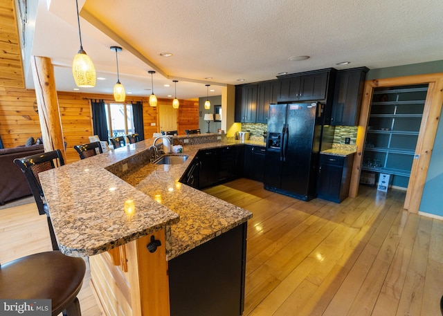 kitchen featuring black fridge, a sink, light stone counters, open floor plan, and light wood finished floors