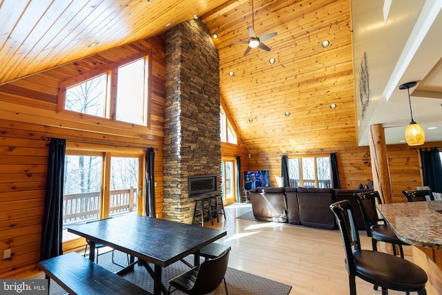 dining space with high vaulted ceiling, wooden walls, a stone fireplace, light wood finished floors, and wood ceiling