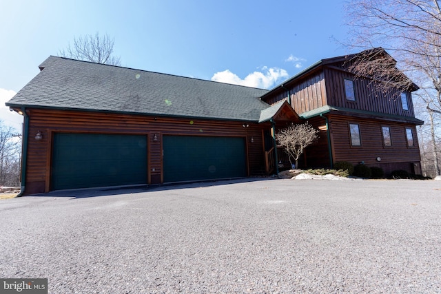 chalet / cabin with aphalt driveway, a garage, and a shingled roof