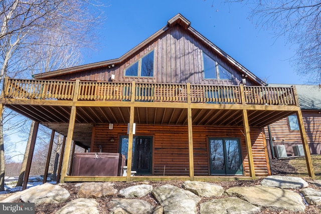 back of house featuring a wooden deck, a hot tub, and log veneer siding