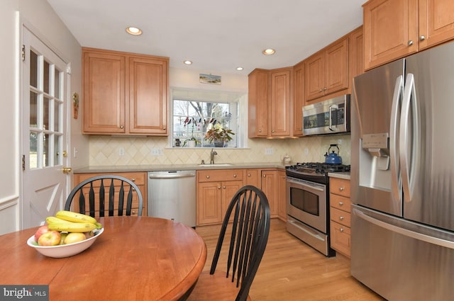 kitchen featuring tasteful backsplash, recessed lighting, light wood-style flooring, stainless steel appliances, and a sink