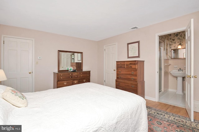 bedroom with visible vents, ensuite bathroom, baseboards, and wood finished floors