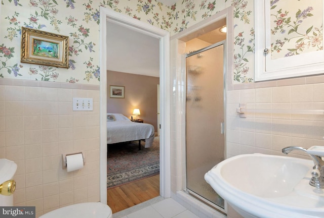 ensuite bathroom with a sink, a wainscoted wall, tile walls, and wallpapered walls