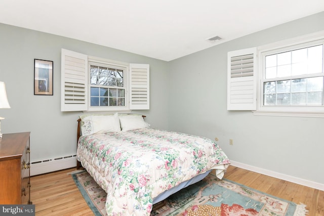 bedroom featuring a baseboard radiator, multiple windows, visible vents, and wood finished floors