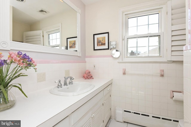 bathroom with visible vents, vanity, baseboard heating, wainscoting, and tile walls