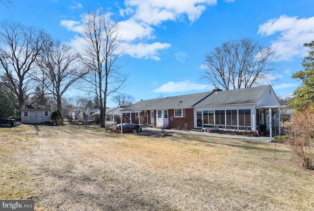 rear view of property featuring brick siding, a chimney, a yard, and a sunroom