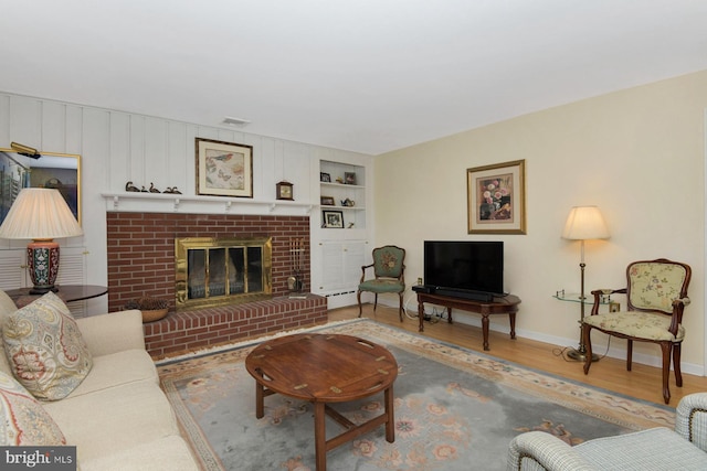 living room featuring visible vents, built in shelves, wood finished floors, a fireplace, and baseboards