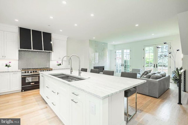 kitchen featuring a sink, white cabinets, french doors, light wood-type flooring, and high end stainless steel range oven