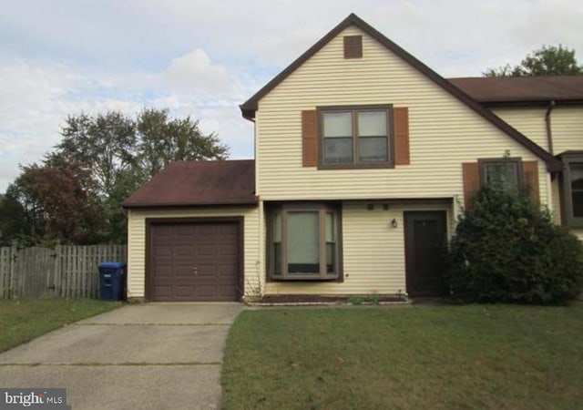 traditional-style home featuring a front yard, concrete driveway, fence, and an attached garage