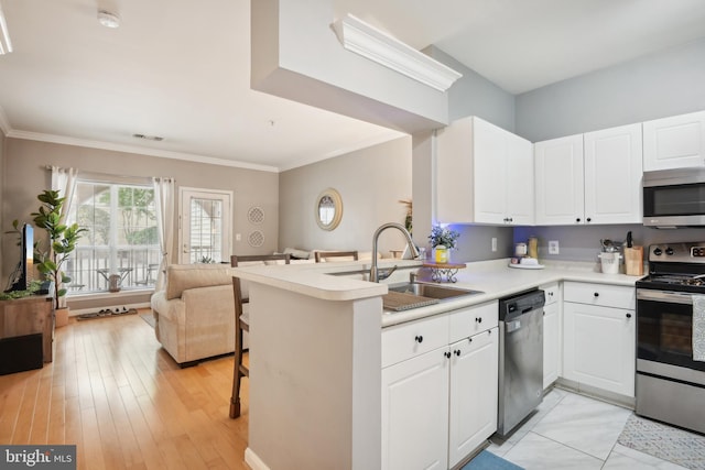 kitchen featuring open floor plan, appliances with stainless steel finishes, white cabinetry, and a sink