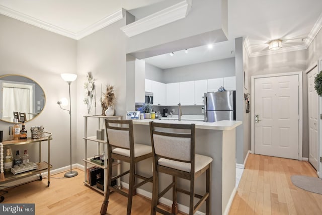 kitchen with appliances with stainless steel finishes, a breakfast bar, crown molding, and light wood finished floors