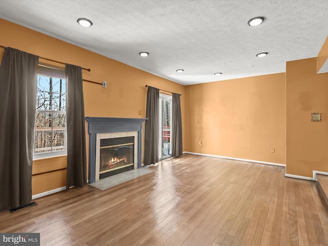 unfurnished living room with a fireplace with flush hearth, wood-type flooring, and baseboards