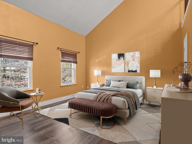 bedroom with high vaulted ceiling, a textured ceiling, baseboards, and wood finished floors