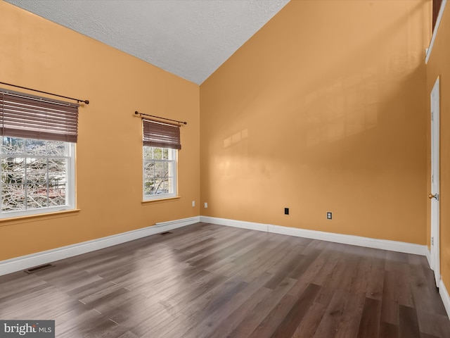 spare room with vaulted ceiling, a textured ceiling, dark wood finished floors, and baseboards