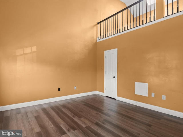 unfurnished room featuring dark wood-style flooring, a towering ceiling, and baseboards