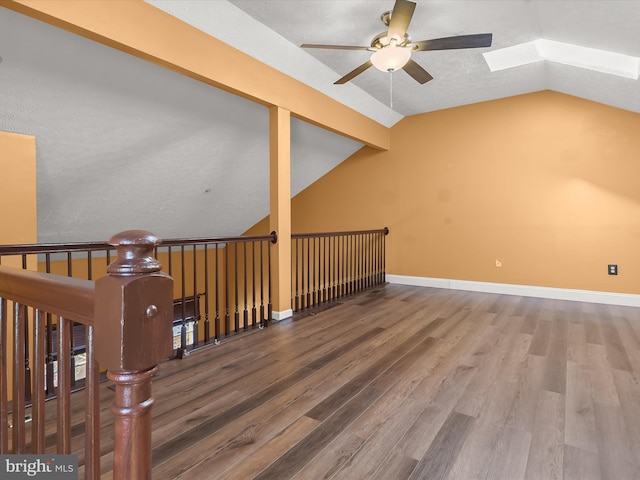 additional living space featuring a ceiling fan, vaulted ceiling with skylight, baseboards, and wood finished floors