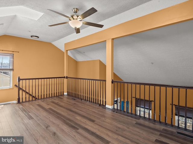 spare room featuring vaulted ceiling with skylight, baseboards, visible vents, wood finished floors, and a textured ceiling