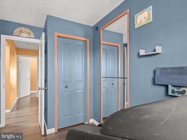 bedroom with a closet, a textured ceiling, baseboards, and wood finished floors