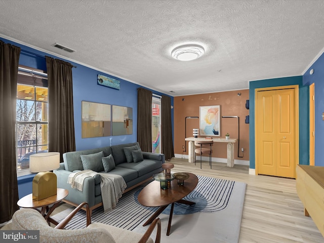 living room with visible vents, ornamental molding, a textured ceiling, light wood-type flooring, and baseboards