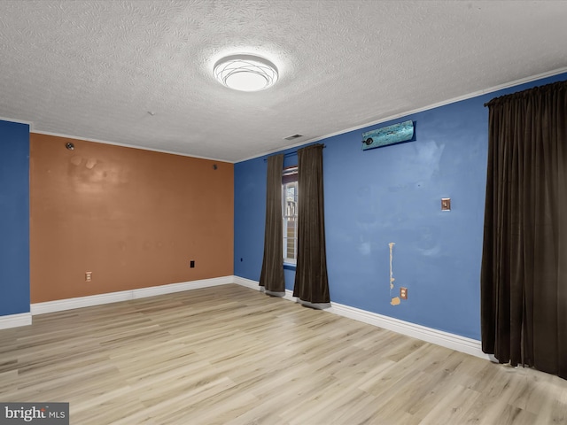 empty room featuring a textured ceiling, wood finished floors, visible vents, and baseboards