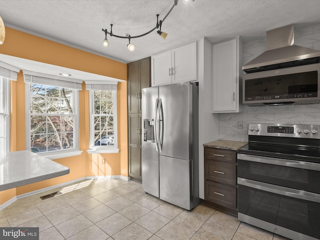 kitchen featuring decorative backsplash, wall chimney exhaust hood, appliances with stainless steel finishes, light stone counters, and white cabinetry