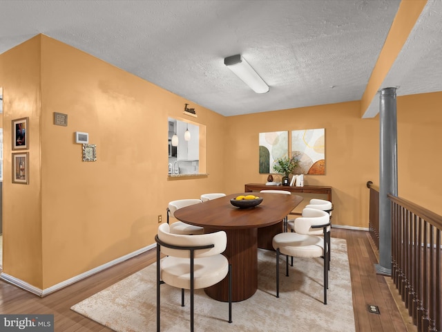 dining space featuring a textured ceiling, baseboards, and wood finished floors