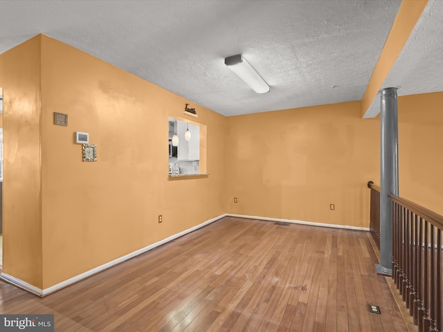 spare room featuring a textured ceiling, hardwood / wood-style floors, and baseboards