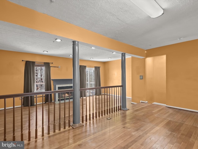 unfurnished room featuring a lit fireplace, a textured ceiling, baseboards, and hardwood / wood-style floors