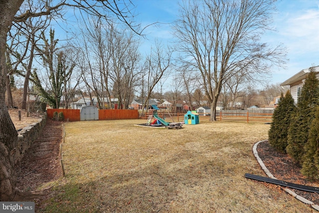 view of yard featuring a playground, an outdoor structure, fence, and a shed