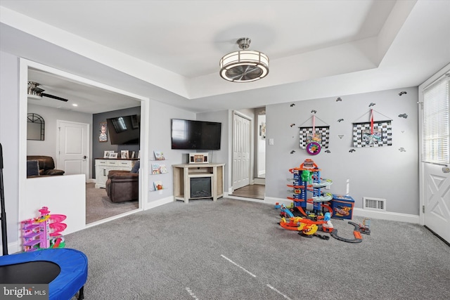 recreation room with carpet floors, a tray ceiling, visible vents, and baseboards