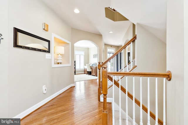 corridor with stairway, wood finished floors, baseboards, recessed lighting, and arched walkways