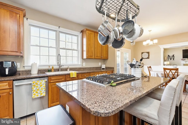 kitchen featuring a center island, light stone countertops, brown cabinets, stainless steel appliances, and a sink