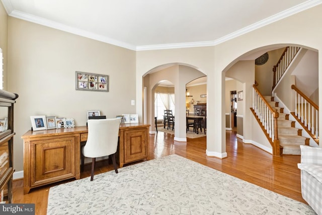 home office with arched walkways, crown molding, light wood-type flooring, and baseboards