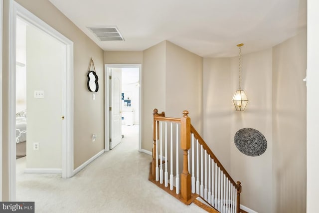 hallway featuring an upstairs landing, visible vents, carpet flooring, and baseboards