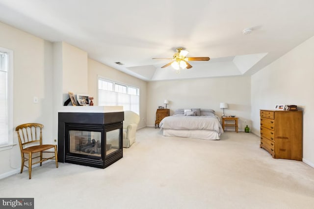 carpeted bedroom with visible vents, baseboards, a multi sided fireplace, a tray ceiling, and a ceiling fan