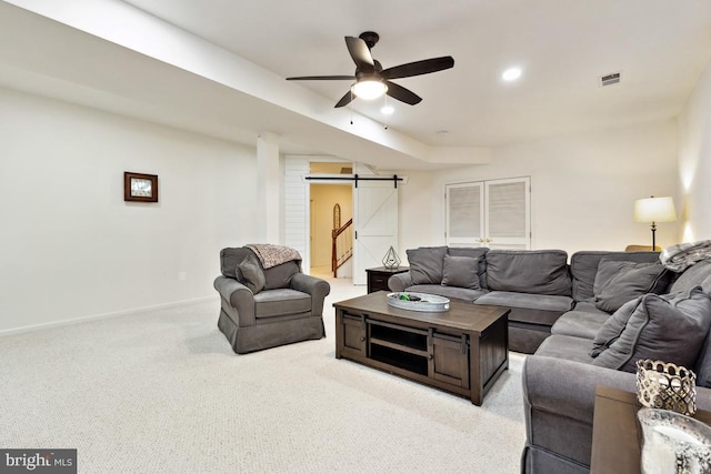 living area featuring visible vents, a ceiling fan, a barn door, baseboards, and light colored carpet