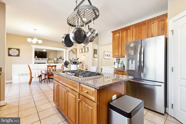 kitchen featuring brown cabinets, stone countertops, a kitchen island, appliances with stainless steel finishes, and light tile patterned floors