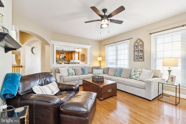 living room featuring arched walkways, baseboards, light wood-type flooring, and ceiling fan