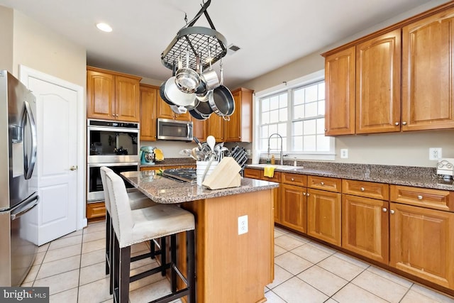 kitchen with a sink, light tile patterned flooring, stone counters, and stainless steel appliances