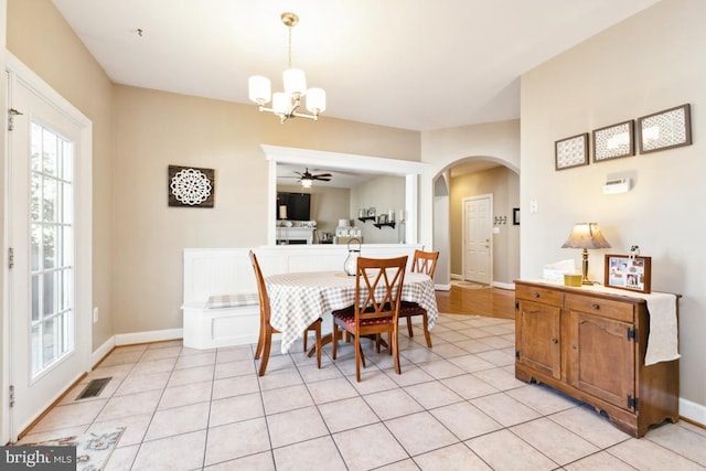 dining room with visible vents, ceiling fan with notable chandelier, arched walkways, light tile patterned flooring, and baseboards