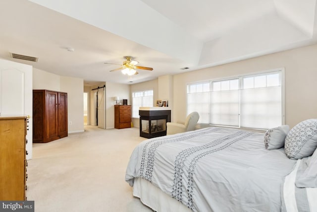 bedroom featuring visible vents, a multi sided fireplace, light carpet, and a ceiling fan