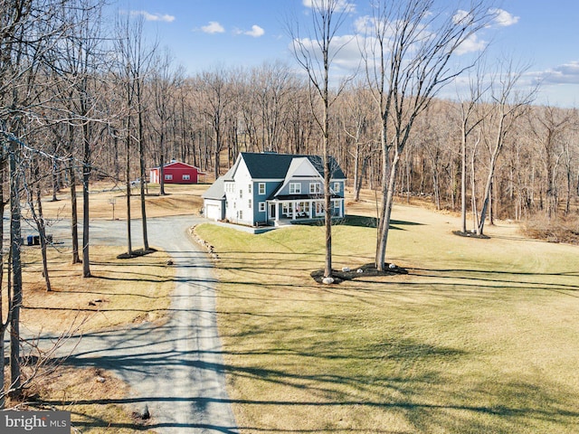 view of front of home with dirt driveway, a porch, a front yard, and a wooded view