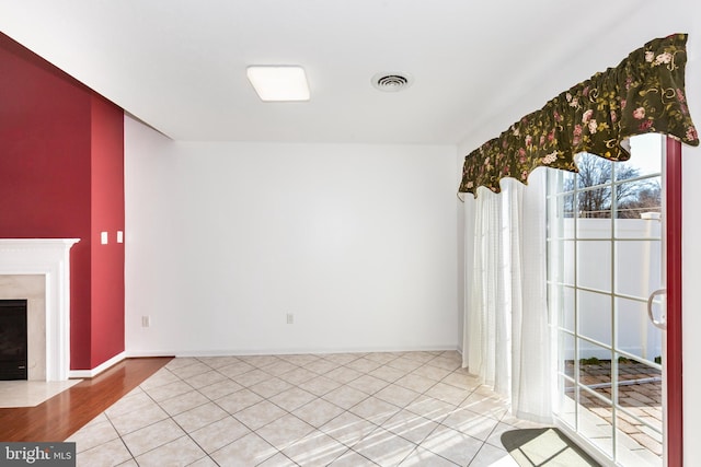 unfurnished living room with light tile patterned floors, visible vents, a fireplace with flush hearth, and baseboards