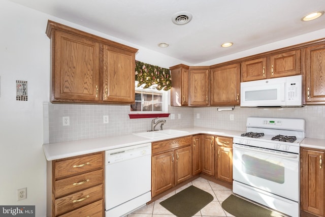 kitchen with brown cabinetry, visible vents, white appliances, and a sink