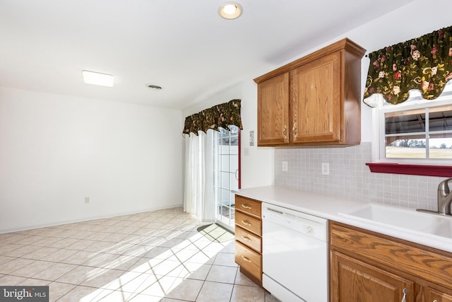 kitchen featuring brown cabinets, a sink, tasteful backsplash, white dishwasher, and light tile patterned floors