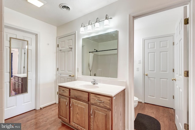 bathroom featuring vanity, wood finished floors, visible vents, a shower, and toilet